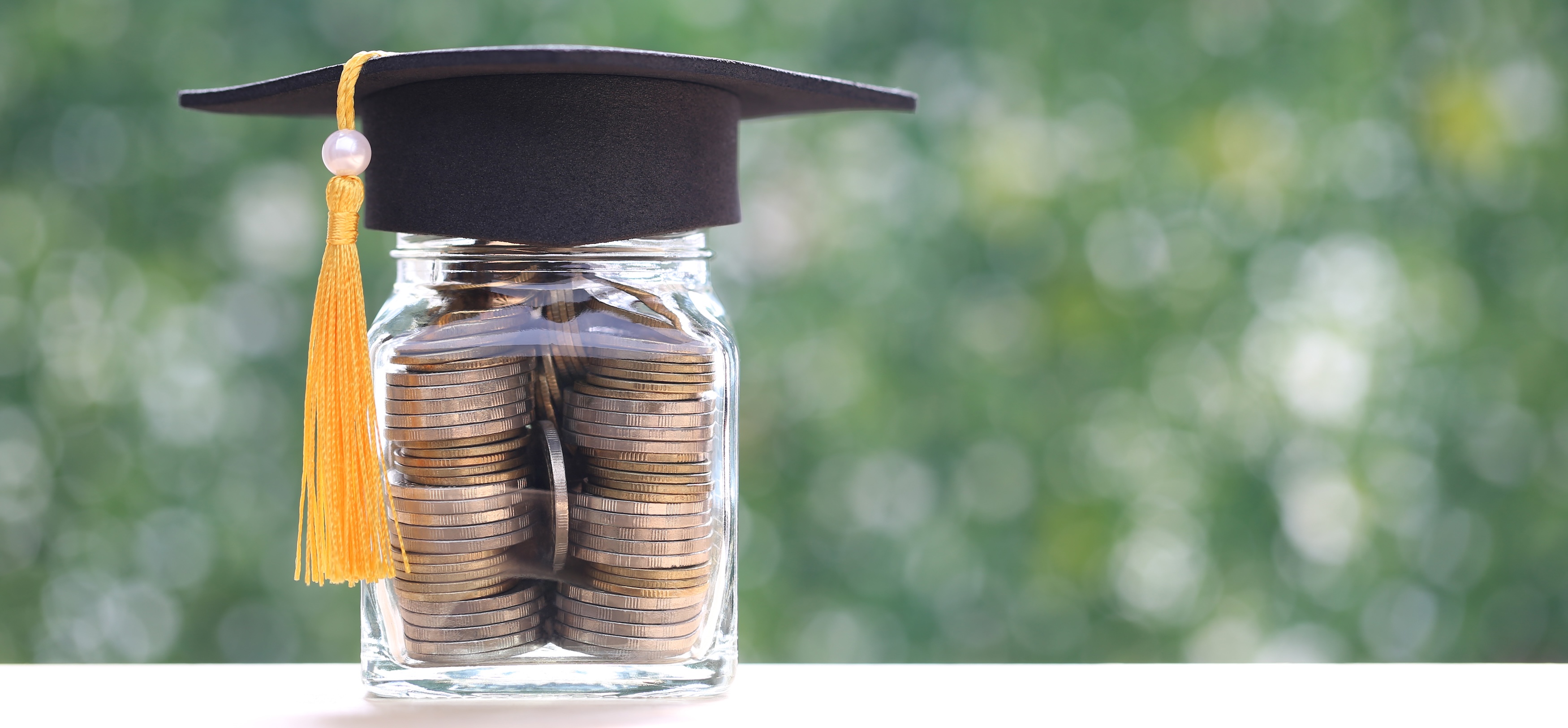Coins in a jar, with graduate cap on top, representing student debt